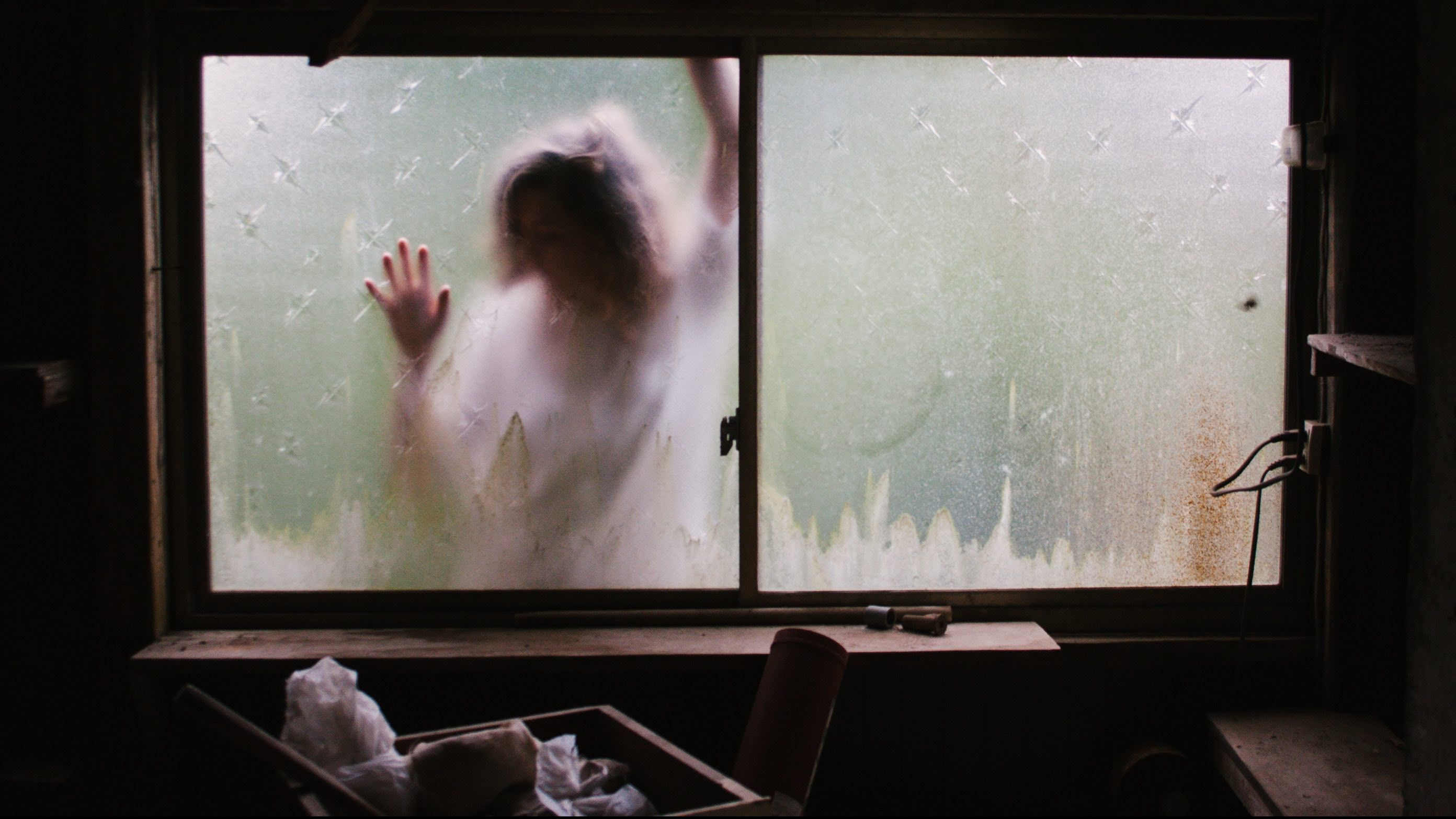 Woman in white trapped outside a frosted window as if trapped outside of her life.